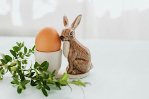 Äggkopp i keramik med en påskhare och ett brunt ägg bredvid gröna kvistar.
